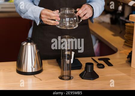 Der Barista dreht sich in den Händen und schaut mit dem Kaffee auf den Topf, bevor er Aeropress macht. Kaffeebrauprozess. Skandinavische Kaffeebrühmethode Stockfoto