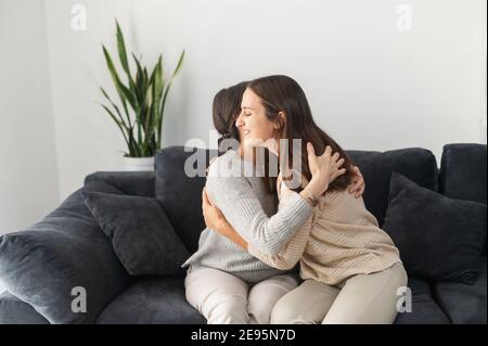 Eine Erwachsene Tochter umarmt eine ältere ältere Mutter auf dem Sofa im gemütlichen Wohnzimmer sitzen, zwei verschiedene Generationen Frauen umarmt drinnen. Familienbande Stockfoto