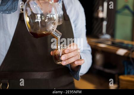 Nahaufnahme Kaffee in doppelter Glastasse im Café von einem hübschen Barista mit Bart. Kaffee Brühsystem und Aeropress alternative Methoden. Werbung für s Stockfoto