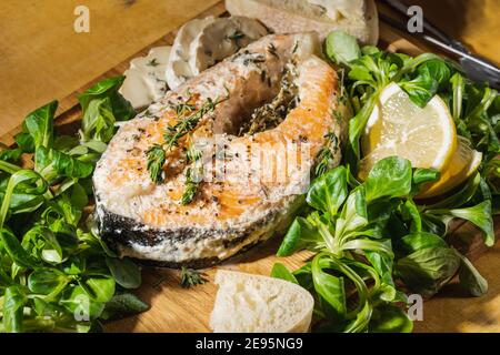 Gebackenes Lachssteak mit Thymian und Sahnesauce, Maissalat, Brot und Blauschimmelkäse auf rustikalem Holzbrett direkt darüber. Lieblingsessen, gesunde Ernährung Stockfoto