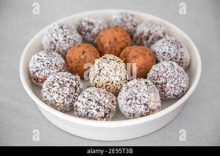 Handgemachte Kokosnussschneebälle aus Datteln, Mandel- und Kokosnusstrüffel auf grauer Oberfläche Stockfoto