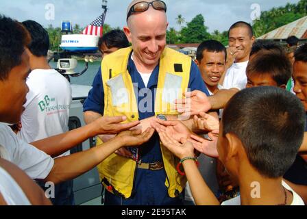 Chief Warrant Officer Marc Manor übergibt Süßigkeiten an einige der Stadtbewohner aus dem kleinen Dorf Leloan, während Besatzungen vom Amphibiendock-Landungsschiff USS Harpers Ferry (LSD 49) am 20. Februar 2006 eine Stranduntersuchung durchführen. DIE US-Marine leistet humanitäre Hilfe für die Opfer in der Gemeinde Saint Bernard, wo die Stadt Guinsahugon im südlichen Teil der Insel während eines Erdrutsches vom 17. Februar vollständig zerstört wurde. Foto USN über ABACAPRESS.COM Stockfoto