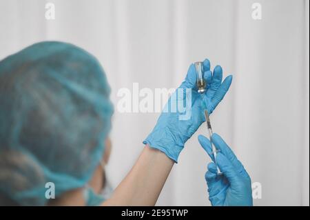 Die Hand einer Krankenschwester in blauen Nitrilhandschuhen zieht einen Impfstoff in eine Spritze. Coronavirus-Impfkonzept mit Spritze und blauen Handschuhen. Stockfoto