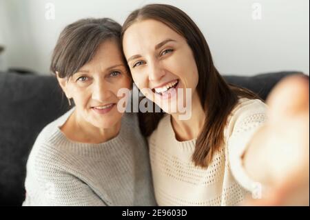 Eine Erwachsene Tochter und eine ältere Mutter machen ein Selfie, zwei lächelnde Generationenfrauen schauen fröhlich auf die Kamera, nehmen sich auf Stockfoto