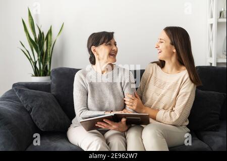 Zwei Frauen unterschiedlichen Generationen verbringen Freizeit zu Hause, eine ältere Mutter und eine Erwachsene Tochter schaut Bilder im Fotoalbum zusammen, erinnern Sie sich Stockfoto