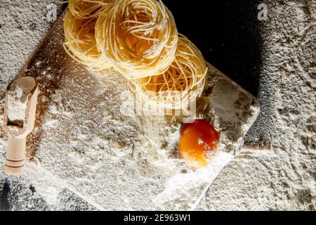 Frisch gekochte Pasta liegt auf einer dunklen, mit Mehl bestäubten Oberfläche. Italienische Pasta. Tagliatelle. Rohe Pasta. Italienische Pasta Rezept. Draufsicht, Kopierbereich. Stockfoto