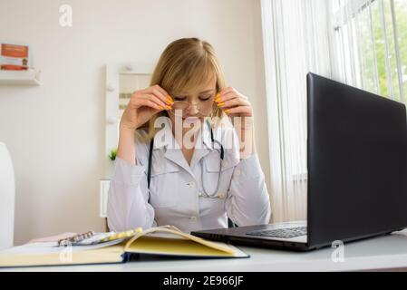 Junge gestresste Frau Arzt sitzt in modernen Office.Tired Arzt am Computer. Online-Beratung. Stockfoto