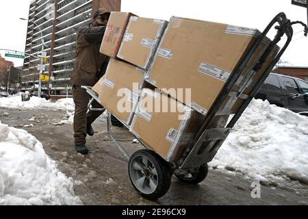 New York, USA. Februar 2021. Ein UPS-Lieferer schiebt einen mit Paketen gestapelten Handwagen bei einem Fußgängerüberweg durch eine Pfütze aus geschmolzenem Schnee, nachdem ein Wintersturm mehr als 17 Zoll Schnee in Teile der Stadt gebracht hatte, im Stadtteil Queens von New York City, NY, 2. Februar 2021. (Foto von Anthony Behar/Sipa USA) Quelle: SIPA USA/Alamy Live News Stockfoto