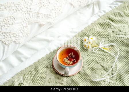 tasse natürlichen Kräutertee aus Minze und Zitronenmelisse im Bett, am Morgen Nahaufnahme. Gemütliche Atmosphäre. Diagonale Spitze, weiße Baumwolldecke, Sommer Gänseblümchen Blumen Stockfoto