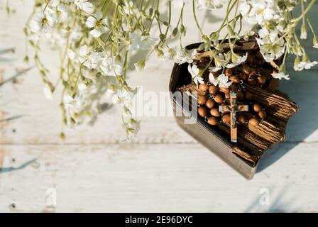 Hände gefaltet im Gebet über alte Bibel. Holzhintergrund.Hände und Rosenkranz, Gebet, Buch mit gelben Seiten. Weiße Blumen auf einem Hintergrund. In der Stockfoto