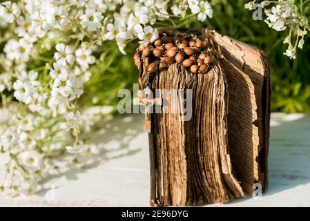 Hände gefaltet im Gebet über alte Bibel. Hölzerner Hintergrund.Hände und Rosenkranz, Gebet, altes Buch mit gelben Seiten. Weiße Blumen auf einem Hintergrund. In Stockfoto