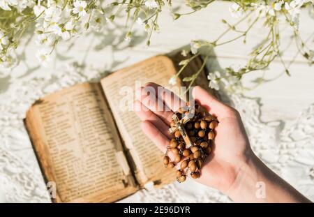 Hände gefaltet im Gebet über alte Bibel. Hölzerner Hintergrund.Hände und Rosenkranz, Gebet, altes Buch mit gelben Seiten. Weiße Blumen auf einem Hintergrund. In Stockfoto