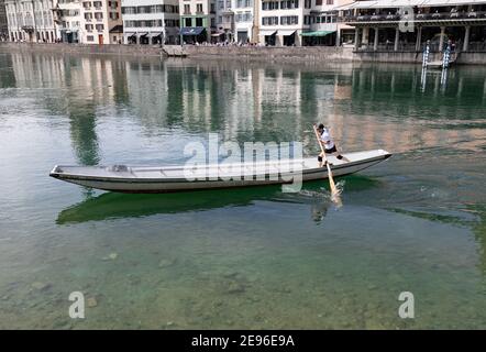 zürich, schweiz - 25. april 2019: Ein junger Mann in einem weißen T-Shirt paddelt in einem langen Ruderboot entlang der limmat, der blau-grüne Fluss ist V Stockfoto