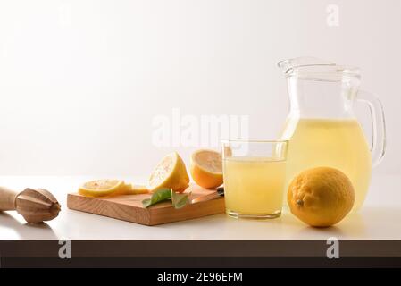 Krug und Glas gefüllt mit frisch gepresstem Zitronensaft mit geschnittenem Obst auf Schneidebrett isoliert weiß. Vorderansicht. Horizontale Zusammensetzung. Stockfoto