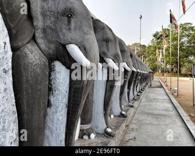 ANURADHAPURA, SRI LANKA - 9. März 2019: Linie von geschnitzten Elefanten schützen die Ruwanwelisaya Stupa in der heiligen Stadt Anuradhapura. Horizontale Aufnahme. Stockfoto