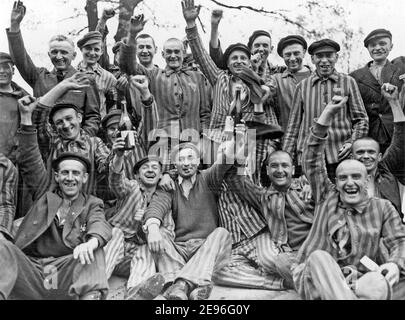 Polnische Häftlinge im Nazi-Konzentrationslager Dachau in Deutschland feiern freudig ihre Befreiung durch die US-Armee. Der Mann, der in der Mitte zwischen den Flaschen steht, trägt ein P-Dreieck, April 1945 Stockfoto