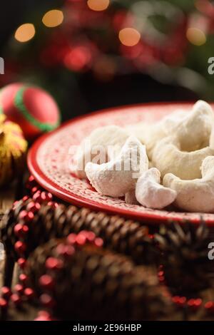 Traditionelles österreichisches Weihnachtsgebäck: Vanillekipferl. Hausgemachte Nussgebäck in Puderzucker auf rotem Teller mit Tannenzapfen Kopie dekoriert Stockfoto