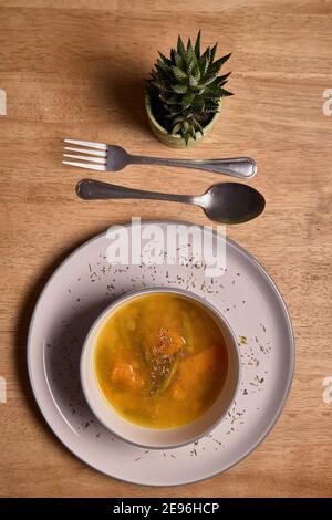 Gemüsesuppe oder Brühe mit Kürbis und Kichererbsen in einer Schüssel. Feine Streukräuter. Massivholz Hintergrund. Gesundes, veganes und diätetische Lebensmittel Stockfoto