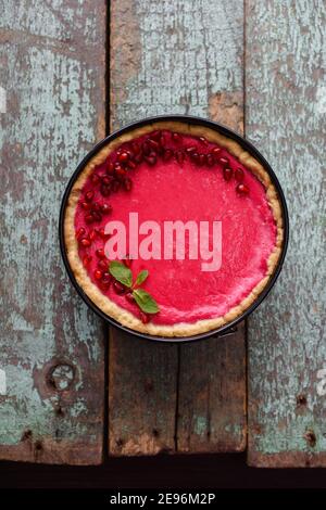 Rosa Dessert in hellen Farben. Hausgemachter Preiselbeerkuchen mit Granatapfelkernen und Minze auf alten schäbigen blauen Brettern Draufsicht Copyspace Stockfoto