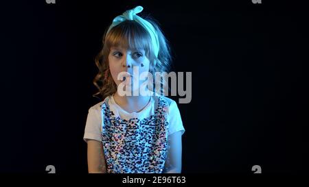 Elegantes Kind Kind in Neonbeleuchtung posiert bei Disco Party Cyberpunk Studio. Futuristische Hipster Teenager Kinder machen Gesichter. Portrait von trendy stilvolle Mädchen zeigt Zunge, um zu täuschen. Stockfoto