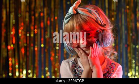 Portrait von trendy stilvolle Mädchen mit Blick auf die Kamera, lächelnd. Nettes Kind Kind in roten Neonbeleuchtung posiert in Disco Cyberpunk Club. Futuristische Hipster Teenager Kinder machen Gesichter, um zu täuschen Stockfoto