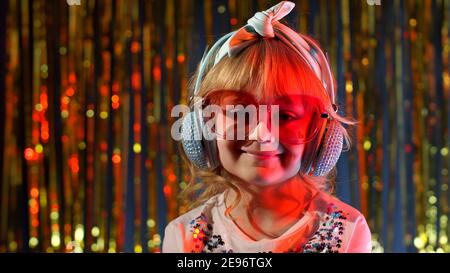 Portrait von trendy stilvolle Mädchen mit Blick auf die Kamera, lächelnd. Nettes Kind Kind in roten Neonbeleuchtung posiert in Disco Cyberpunk Club. Futuristische Hipster Teenager Kinder machen Gesichter, um zu täuschen Stockfoto