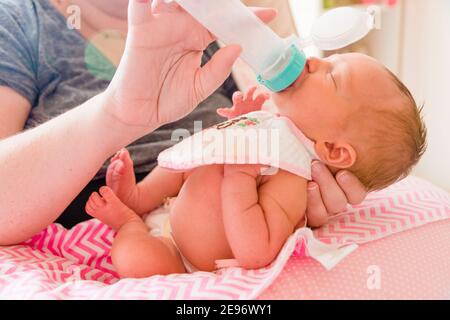 Mutter hält und Fütterungsflasche für neugeborenes Mädchen im Zimmer des Babys. Stockfoto