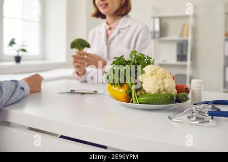 Positive Frau Arzt Ernährungswissenschaftler im Gespräch mit Mann Patient über Vorteile Von frischer veganer gesunder Ernährung Stockfoto