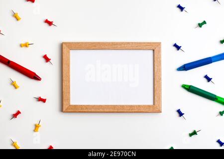 Gelb rot blau grün Stecknadeln, Holzrahmen und Stifte links und rechts auf weißem Hintergrund. Flache Lay-Ansicht von oben. Bildung zurück in die Schule und onli Stockfoto