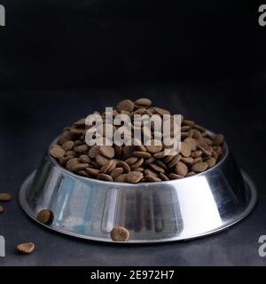 Trockenes Hundefutter in Metallschüssel auf dunklem Hintergrund Stockfoto