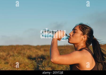 Seitenansicht der Frau, die nach sportlichen Aktivitäten Wasser trinkt. Speicherplatz kopieren Stockfoto