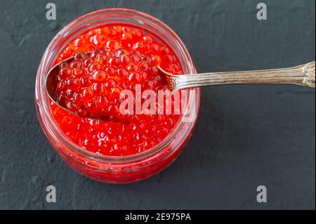 Roter Kaviar im Glas mit silbernem Löffel. Meeresfrüchte. Gesunde Ernährung. Diät. Schwarzer Hintergrund Stockfoto