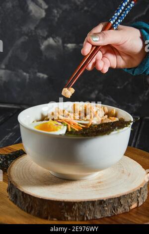 Junge Japanerin beim Abendessen schmeckt köstlich udon Ramen - japanische Ramen-Suppe mit Huhn, Ei, Knoblauch und Nudeln auf dunklem Holzgrund Stockfoto