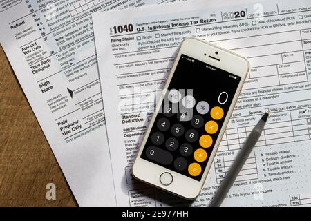 Das Formular 1040, US-Einkommensteuererklärung für das Jahr 2020, ein iPhone zeigt den Rechner App-Bildschirm, und ein Stift sind auf einem Schreibtisch zu sehen. Stockfoto