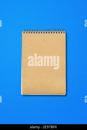 Spiral geschlossenes Notebook-Modell, brauner Papierdeckel, isoliert auf blauem Hintergrund Stockfoto