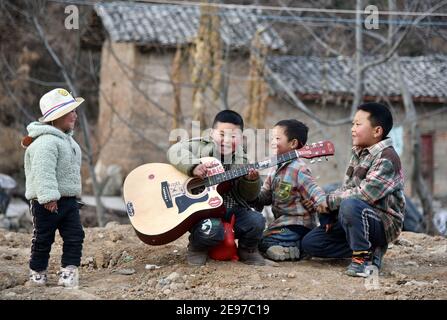 (210203) -- LIANGSHAN, 3. Februar 2021 (Xinhua) -- Wuqi Buji (2nd L), Sohn von Bamu Yubumu, spielt Gitarre in der Nähe seines Wohnsitzes im Dorf Taoyuan, Bezirk Yuexi, Autonome Präfektur Liangshan Yi, südwestlich der Provinz Sichuan, 20. Januar 2021. Eine junge Mutter lehnte sich mühsam nach vorne, um das Gewicht eines übergroßen Gepäcks auf ihrem Rücken und eines kleinen Babys in ihrem Arm auszugleichen, als sie ihre Schritte nach vorne kämpfte. Dies war das Bild, das der Xinhua Reporter Zhou Ke am 30. Januar 2010 in der Nähe des Nanchang Bahnhofs in Nanchang, der ostchinesischen Provinz Jiangxi, einnahm. Das Foto mit dem Titel „Baby, Mama nimmt dich nach Hause“ Stockfoto