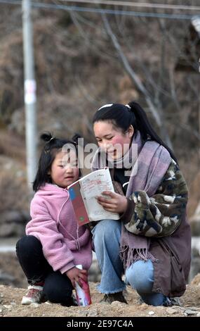 (210203) -- LIANGSHAN, 3. Februar 2021 (Xinhua) -- Wuqi Labumu (R), die älteste Tochter von Bamu Yubumu, liest mit ihrer jüngeren Schwester im Dorf Taoyuan, Bezirk Yuexi, Autonome Präfektur Liangshan Yi, südwestlich der Provinz Sichuan, 20. Januar 2021. Eine junge Mutter lehnte sich mühsam nach vorne, um das Gewicht eines übergroßen Gepäcks auf ihrem Rücken und eines kleinen Babys in ihrem Arm auszugleichen, als sie ihre Schritte nach vorne kämpfte. Dies war das Bild, das der Xinhua Reporter Zhou Ke am 30. Januar 2010 in der Nähe des Nanchang Bahnhofs in Nanchang, der ostchinesischen Provinz Jiangxi, einnahm. Das Foto mit dem Titel 'Baby, Mama nimmt Yo Stockfoto