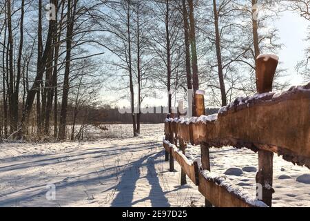 Holzzaun in einer ländlichen Winterlandschaft. Winter Landstraße. Polnischer Februar in Mazovia. Reise nach Europa. Bäume zwischen schneebedeckten Feldern. Stockfoto