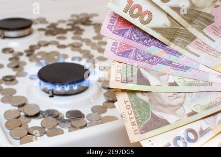 Ukrainische Griwnie vor dem Hintergrund von Münzen und Gasbrennern auf dem Herd. Preis für Gas und Versorgungsunternehmen Stockfoto