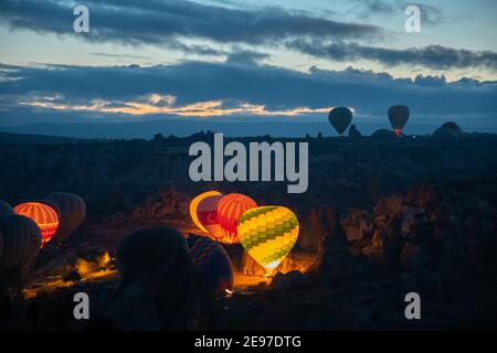 Heißluftballons glühen im Dunkeln am frühen Morgen beim Aufblasen auf Land der Berglandschaft in Kappadokien Türkei. Bunt beleuchtete Luftballons A Stockfoto