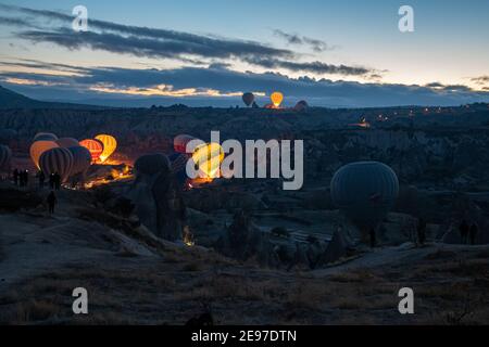 Heißluftballons glühen im Dunkeln am frühen Morgen beim Aufblasen auf Land der Berglandschaft in Kappadokien. Bunt beleuchtete Luftballons unter vo Stockfoto