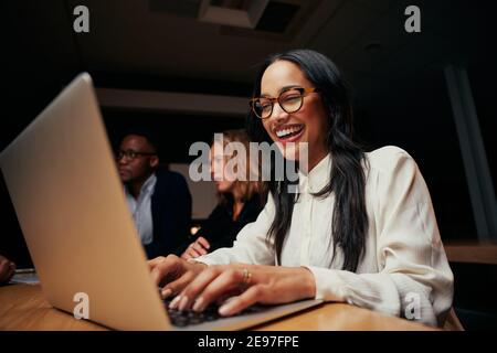 Nahaufnahme der erfolgreichen lächelnden jungen afroamerikanischen Geschäftsfrau, die in der Nähe sitzt Kollegen, die im Büro einen Laptop verwenden Stockfoto