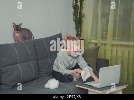 kaukasisches Mädchen lernt Stricken, Anschauen von Unterrichtsvideos auf einem Laptop Klassen in Quarantäne Stockfoto
