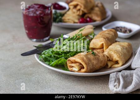 Hausgemachte gefüllte dünne Pfannkuchen oder Crepes mit Fleisch, würzige Cranberry-Sauce und Rucola, hellen Stein Hintergrund. Traditionelle russische Küche für Masleni Stockfoto