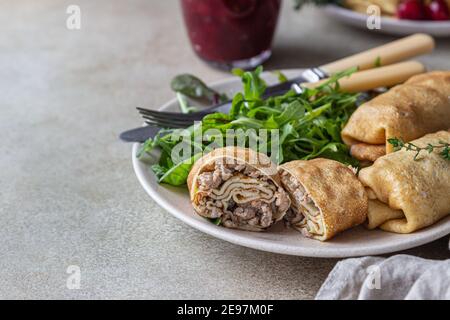 Hausgemachte gefüllte dünne Pfannkuchen oder Crepes mit Fleisch, würzige Cranberry-Sauce und Rucola, hellen Stein Hintergrund. Traditionelle russische Küche für Masleni Stockfoto