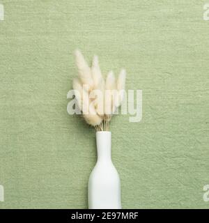 Vase aus beigem Lagurus ovatus trockenes Gras auf grünem Stoff Hintergrund. Flach legen, Draufsicht, Kopierraum Stockfoto