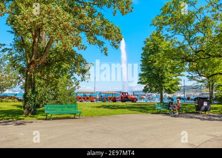 Genf, Schweiz - 15. Aug 2020: Roter Touristenzug mit Waggons und Lokomotive entlang der Promenade du Lac in Jardin Anglais mit Jet d'Eau Stockfoto