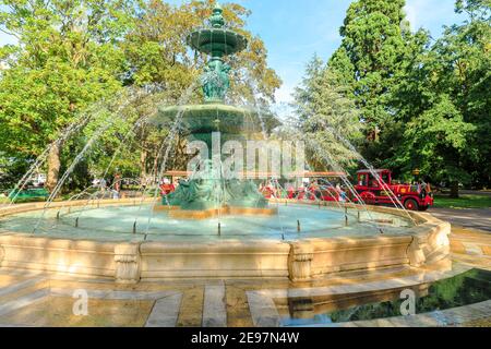 Genf, Schweiz - 15. Aug 2020: Brunnen der vier Jahreszeiten im Zentrum von Jardin Anglais mit rotem Touristenzug mit Waggons und Lokomotive Stockfoto