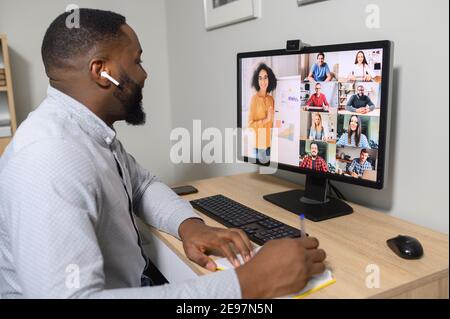 Seitenansicht ein Afrikaner spricht online mit einer Gruppe verschiedener Mitarbeiter, Kollegen auf dem Laptop-Bildschirm, Videoanruf, Online-Meeting. App für Stockfoto