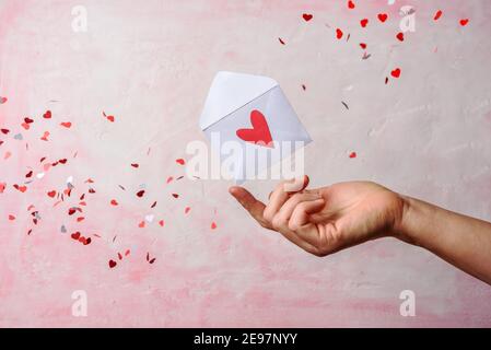 Umschlag auf der Hand mit fliegenden roten Herzen auf rosa Hintergrund. Valentinstag Stockfoto